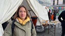 Eine Frau steht vor einem Protestcamp-Zelt in einer Innenstadt.