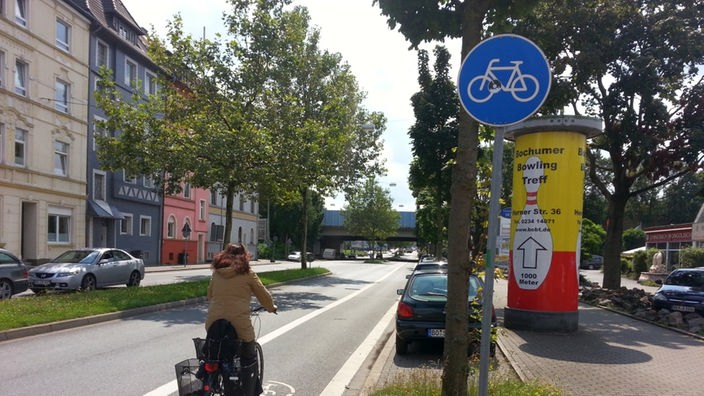 Radfahrerin radelt auf dem eingezeichneten Radweg an der Seite einer größeren Straße