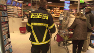 Mann mit Feuerwehrmontur und Einkaufswagen geht vorbei an anderen Kunden gleich zur Kasse