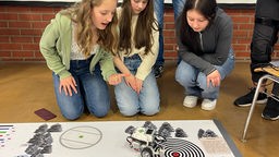 Drei Schülerinnen verfolgen mit gespannten Mienen ihren Roboter