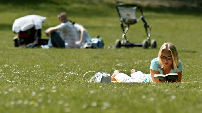 Eine Frau liegt bei sonnigem April-Wetter auf einer Wiese in einem Park in Oberhausen und liest.
