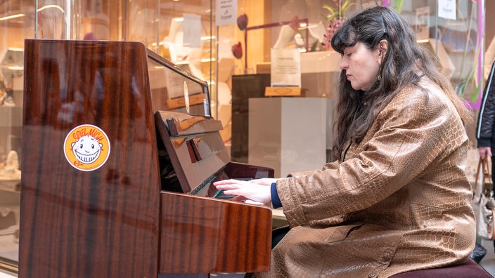 Eine Frau sitzt vor einem Geschäft an einem Klavier und spielt. 
