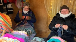 Zwei Frauen stricken in einem Stand auf dem Weihnachtsmarkt. 