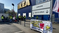 Ikea-Mitarbeiter vor dem Gebäude, davor ein Transparent mit der Aufschrift "Tarifvertrag Zukunft Ikea - entdecke die Möglichkeiten"
