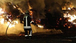 Ein Feuerwehrmann vor brennenden Strohballen