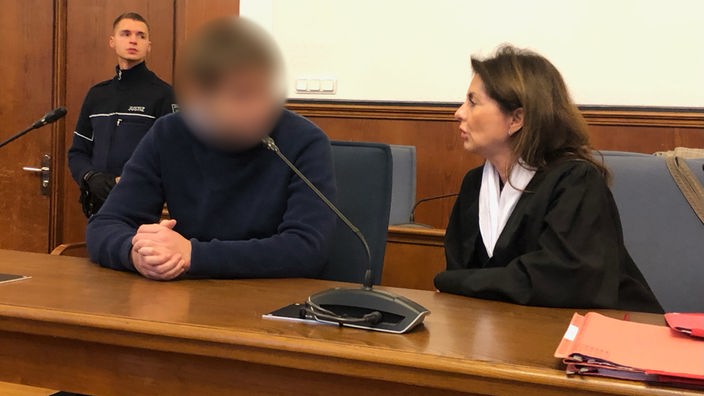 Der Angeklagte der Amoktat in Hamm sitzt neben einer Frau im Gerichtssaal.