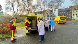 Fünf Personen stehen um einen Ambulanzwagen herum 