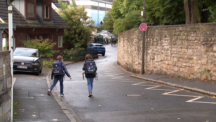 Zwei Kinder mit Schulranzen laufen in Richtung Schule