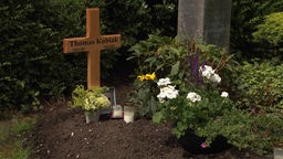 Auf dem frischen Grab stehen ein Holzkreuz, Blumen und Kerzen. 