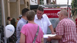 Mann im weißen Hemd am Stehtisch mit Bürgern auf einem Marktplatz