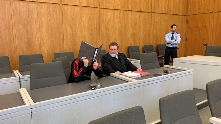 Der Verurteilte verdeckt sich im Gerichtssaal sein Gesicht mit einem schwarzen Ordner.