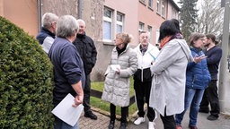 Eine Menschengruppe steht vor einem Wohnhaus und diskutiert. 