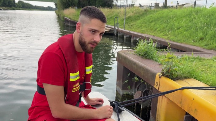 Das Foto zeigt den Rettungsschimmer Julian Bajo in roter DLRG-Kleidung auf einem am Land festgemachten Boot