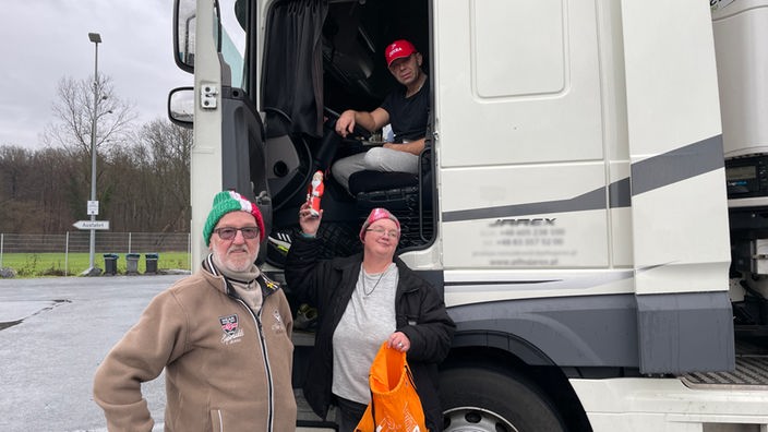Ein Mann und eine Frau vor einer LKW-Fahrerkabine, die Frau hält eiinen Schoko-Nikolaus hoch