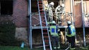 Feuerwehrleute stehen nach dem Löschen an einem abgebrannten Mehrfamilienhaus