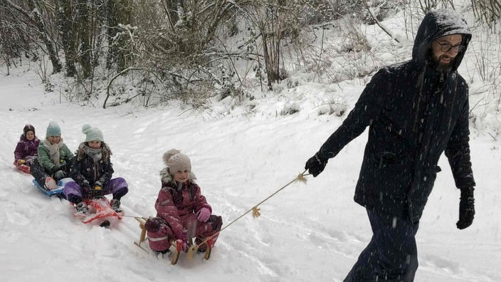 Ein Mann zieht mehrere Kinder auf Schlitten durch den Schnee in Aachen
