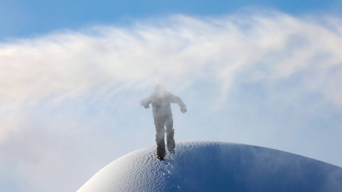 Eine Person auf einem Berg aus Schnee wird von einer Schneekanone beschneit.