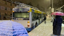 Passanten stehen mit Regenschirmen vor einem verschneiten Bus