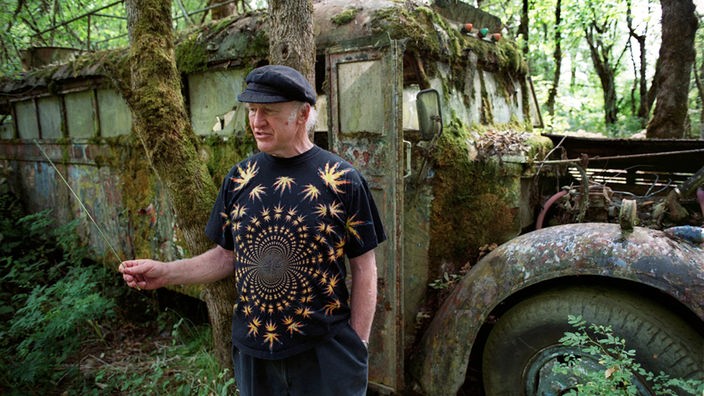Der amerikanische Schriftsteller Ken Kesey steht auf seiner Farm Pleasent Hill vor seinem legendären, ehemals bunt bemalten Bus "Further", der mittlerweile mit Moos bewachsen ist.