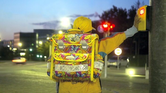 Schulkind bei Dämmerung an der Ampel mit einem Schulranzen auf dem Rücken.