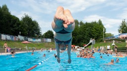 Nordrhein-Westfalen, Bielefeld: Ein Badegast springt von einem Startblock in das Wasserbecken von einem Freibad.