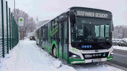 Ein Bus steht an einer Haltestelle, es schneit und es liegt Schnee