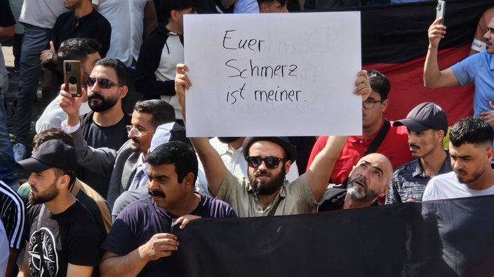 Ein Mann hält ein Schild mit der Aufschrift "Euer Schmerz ist meiner" in die Luft