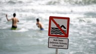 Schild "Nicht Baden - Gefährliche Strömung - Lebensgefahr!", Badegäste im Hintergrund