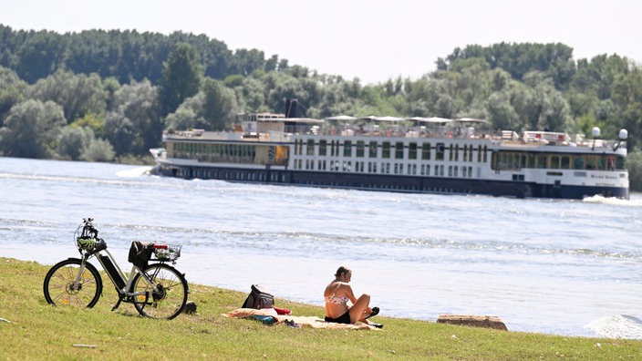 Eine Frau mit Fahrrad sitzt am Rhein