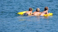 Drei Badegäste schwimmen mit einer Luftmatratze über einen Badesee