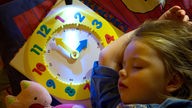 Ein Kind schläft in ihrem Bett mit eingeschalteter Taschenlampe und einer Kinder-Uhr