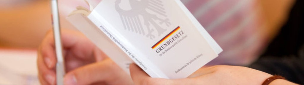 Eine Studentin hält eine Druckversion des Deutschen Grundgesetzes