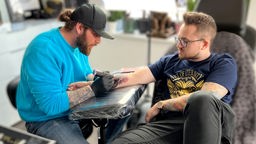 Der Tätowierer Stefan Muler sticht Edwin Großmann ein Tattoo auf die Unterseite des Unterarms.