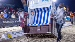 Zwei bärtige Männer schleppen einen Strandkorb über den Sand