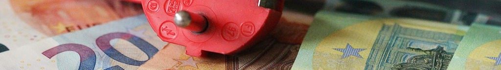 Ein roter Stecker vor einem Zeitschalter und Geldscheinen -  Symbolbild