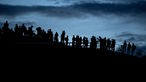 Zahlreiche Menschen stehen auf dem Olympiaberg und schauen sich den Sonnenuntergang bzw. den Mondaufgang an