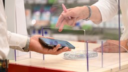 Symbolbild: Eine Person zeigt in einer Apotheke sein Handy
