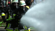 Zwei Feuerwehrleute kämpfen unter Atemschutz mit einem Wasserschlauch gegen Flammen an (Symbolbild)