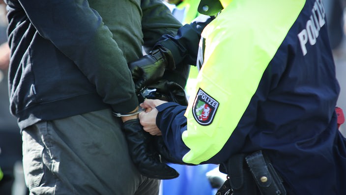 Ein Polizist legt einem vor ihm stehenden Mann Handschellen an (Symbolbild)