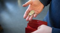 Münzen im Wert von fünf Euro werden über ein rotes Portemonnaie gehalten