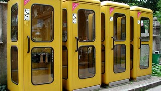 Vier gelbe Telefonzellen stehen nebeneinander im Freien.
