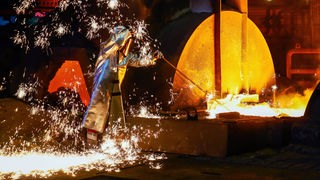 Ein Stahlarbeiter im Schutzanzug entnimmt eine 1.500 Grad heiße Roheisen-Probe beim Abstich am Hochofen.