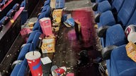 Zwischen den Sitzreihen eines Kinos ist Popcorn verteilt. Außerdem wurden viele Becher und anderer Müll vor Ort gelassen.