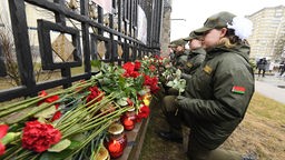 Trauerende in Moskau knieen vor Rosen an einem Zaun
