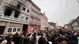 Trauermarsch in Solingen - Menschen stehen vor abgebrannten Gebäude