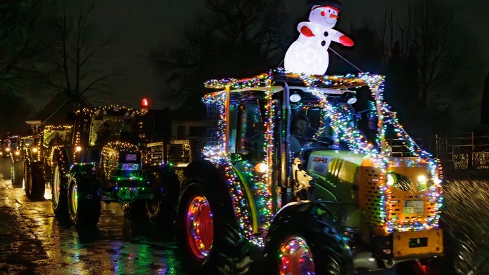 Zu sehen sind mehrere geschmückte, leuchtende Traktoren im Dunkeln - unter anderem mit einem aufblasbaren Schneemann.