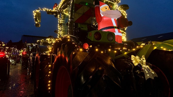 Unter anderem mit einem aufgeblasenen Weihnachtsmann geschmückte und beleuchtete Traktoren in der Dunkelheit.