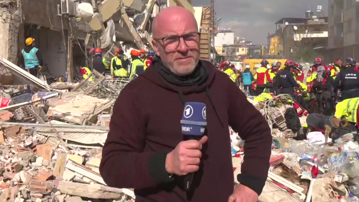 Reporter Jens Eberl steht in der zerstörten Stadt Hatay vor einem eigestürzten Haus.