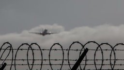 Flugzeug verschwindet in Wolken hinter Stacheldraht