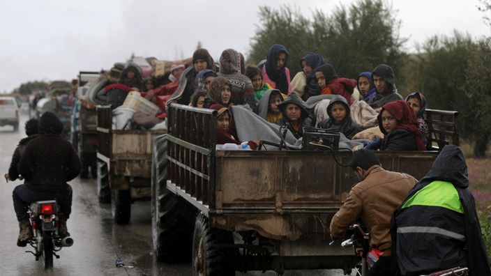 Flüchtlinge sitzen mit Gepäck auf einem offenen Lastwagen auf einer Straße im Nord-Osten von Afrin